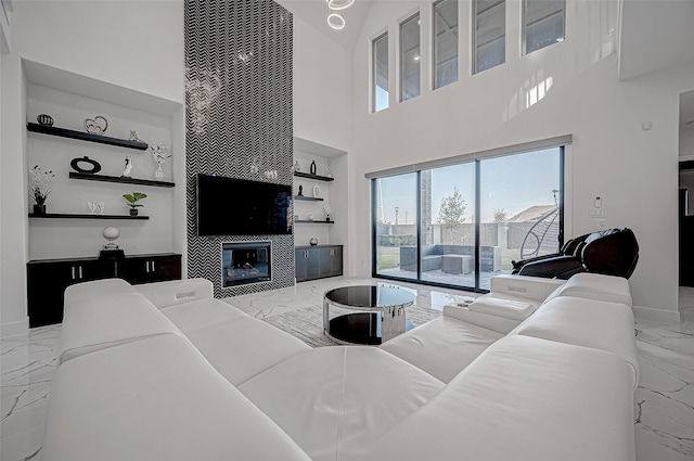 living room featuring a towering ceiling, built in features, and a tiled fireplace