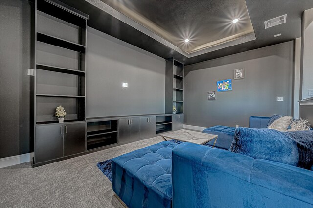 carpeted cinema room featuring a raised ceiling and built in shelves