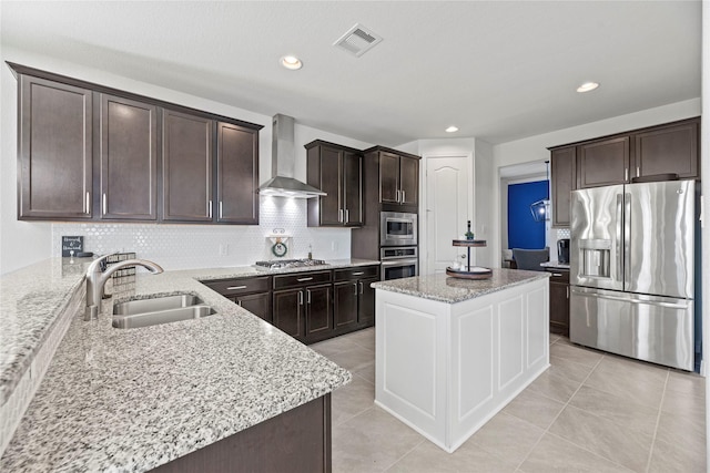 kitchen featuring light stone countertops, stainless steel appliances, wall chimney exhaust hood, and sink