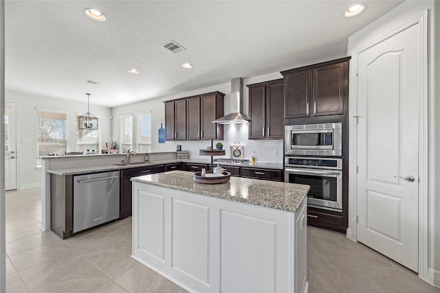 kitchen with sink, appliances with stainless steel finishes, wall chimney range hood, and a center island