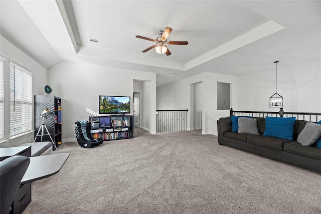 carpeted living room with ceiling fan with notable chandelier and a tray ceiling