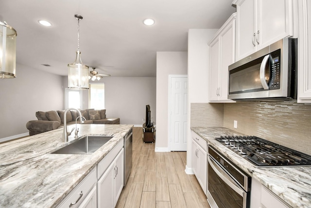 kitchen featuring ceiling fan, stainless steel appliances, white cabinets, light stone counters, and sink