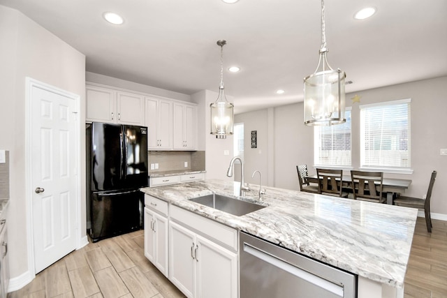 kitchen with black fridge, stainless steel dishwasher, sink, white cabinetry, and a kitchen island with sink