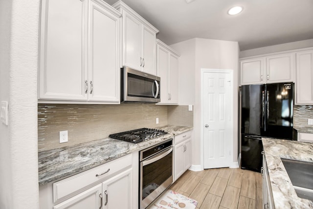 kitchen with stainless steel appliances, white cabinetry, tasteful backsplash, and light stone countertops