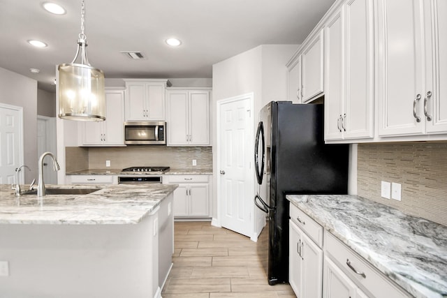 kitchen with appliances with stainless steel finishes, pendant lighting, white cabinets, light stone counters, and sink