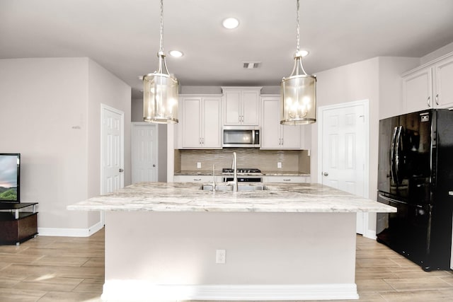 kitchen featuring black fridge, white cabinets, and a kitchen island with sink