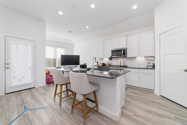 kitchen featuring a kitchen breakfast bar, light hardwood / wood-style flooring, white cabinets, and an island with sink