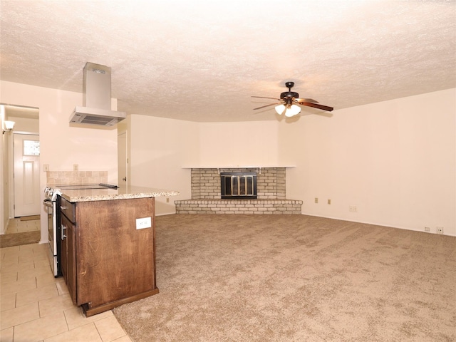 kitchen featuring island range hood, a fireplace, stainless steel range with electric stovetop, ceiling fan, and light carpet