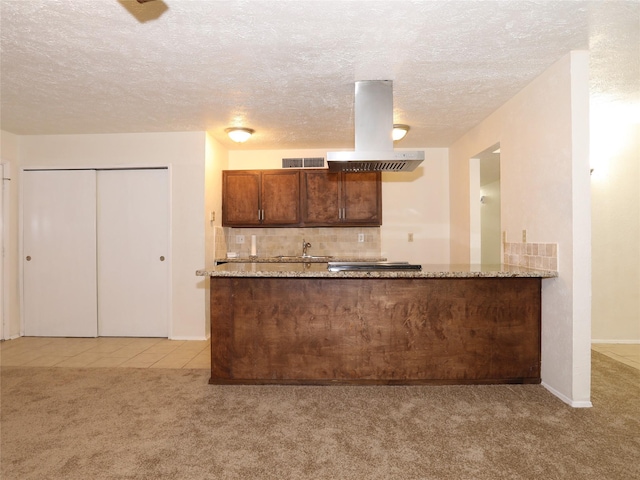 kitchen featuring backsplash, light stone countertops, island exhaust hood, light colored carpet, and kitchen peninsula