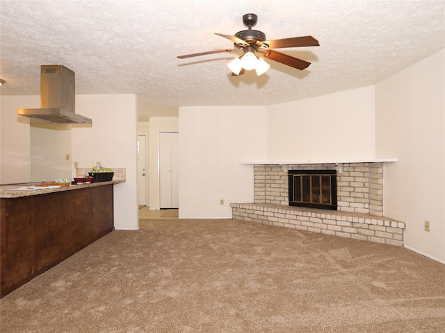 unfurnished living room with ceiling fan, a brick fireplace, light colored carpet, and a textured ceiling