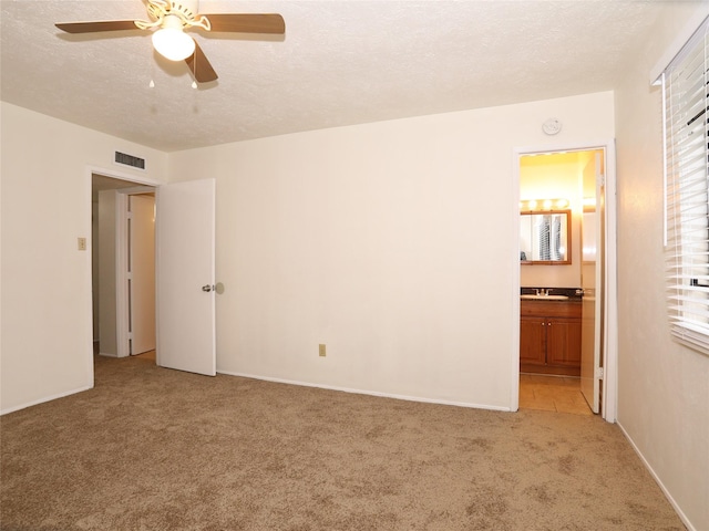 unfurnished bedroom featuring ensuite bathroom, light colored carpet, ceiling fan, and a textured ceiling