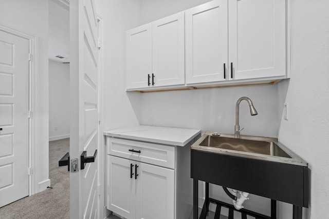 kitchen with white cabinets, light stone countertops, sink, and light colored carpet