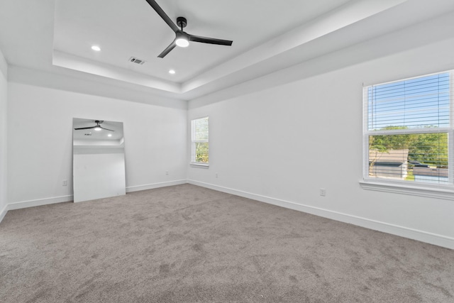 unfurnished bedroom with ceiling fan, a tray ceiling, and carpet flooring