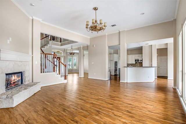 unfurnished living room with light hardwood / wood-style floors, crown molding, and an inviting chandelier