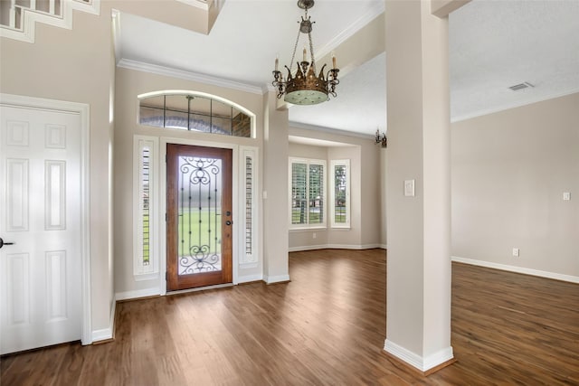 entryway with dark wood-type flooring, ornamental molding, and a notable chandelier