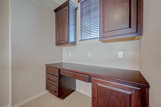 unfurnished office featuring built in desk and light colored carpet