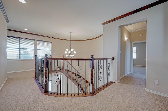 hallway with an inviting chandelier, ornamental molding, a wealth of natural light, and light colored carpet