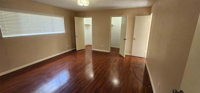 unfurnished bedroom featuring a spacious closet, a closet, and dark hardwood / wood-style flooring