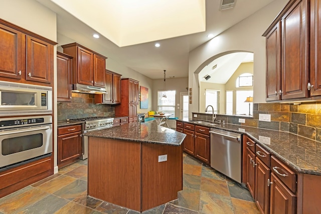 kitchen featuring appliances with stainless steel finishes, a center island, dark stone countertops, decorative backsplash, and sink