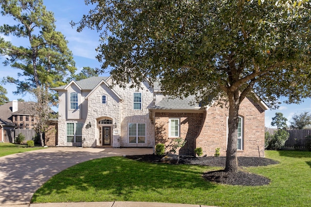 view of front of house with a front yard, fence, roof with shingles, stone siding, and brick siding