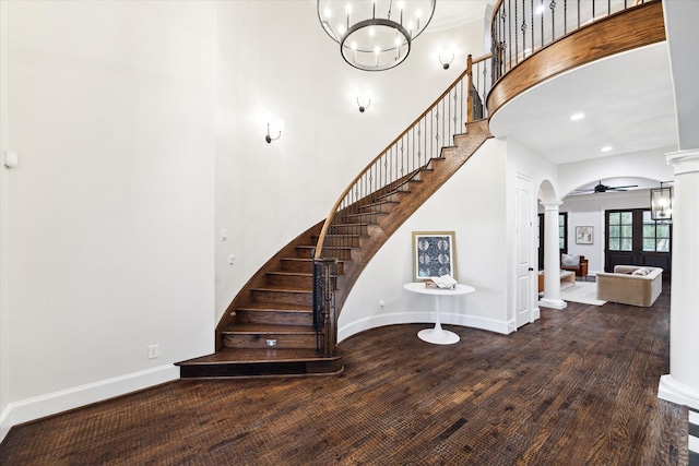 staircase featuring hardwood / wood-style flooring, ceiling fan with notable chandelier, and ornate columns