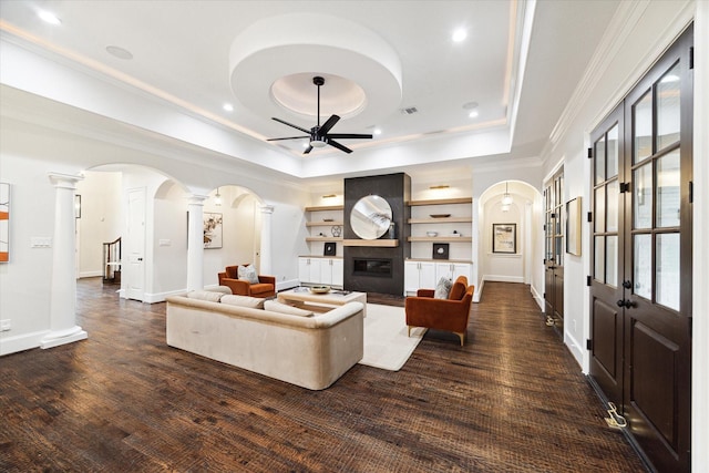 living room featuring ceiling fan, dark hardwood / wood-style floors, crown molding, a tray ceiling, and built in shelves