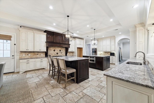 kitchen with decorative light fixtures, a kitchen island, a raised ceiling, sink, and dark brown cabinets