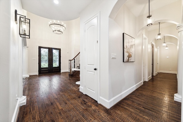 foyer with a towering ceiling, dark wood-type flooring, a chandelier, and french doors