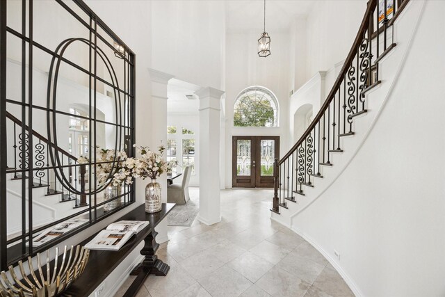 entrance foyer with french doors, a towering ceiling, and ornate columns