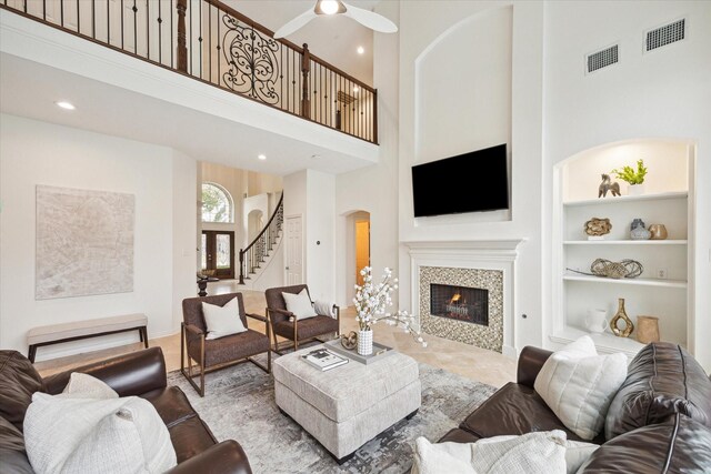 carpeted living room with ceiling fan, a towering ceiling, built in features, and a fireplace