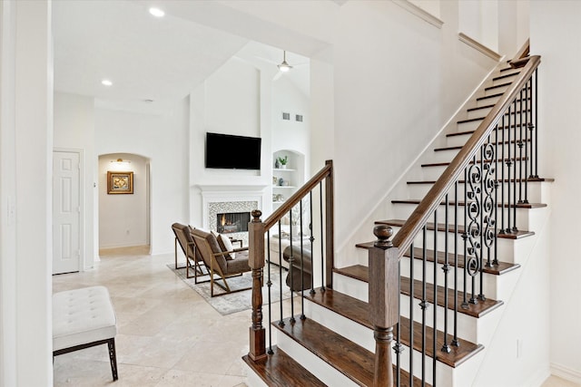 stairway with a tiled fireplace, high vaulted ceiling, ceiling fan, and built in shelves