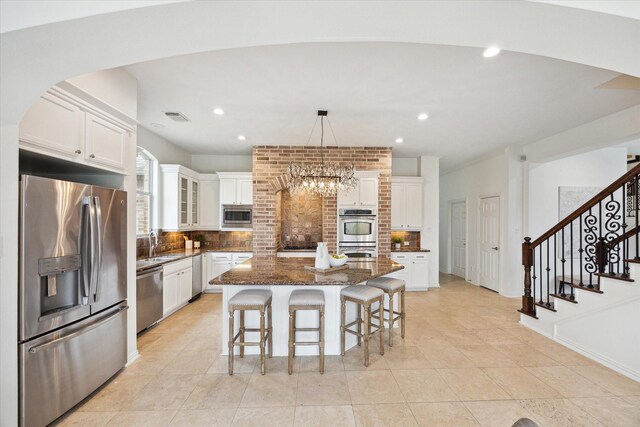 kitchen with sink, stainless steel appliances, white cabinets, a kitchen island, and decorative light fixtures