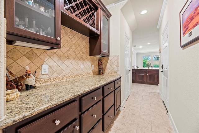 kitchen with backsplash, light stone countertops, crown molding, dark brown cabinetry, and sink