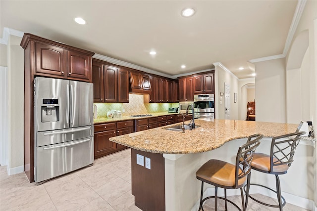 kitchen with a breakfast bar, sink, a kitchen island with sink, light stone countertops, and appliances with stainless steel finishes