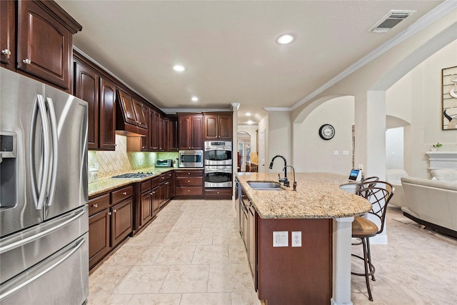 kitchen featuring a kitchen bar, sink, a kitchen island with sink, light stone countertops, and stainless steel appliances