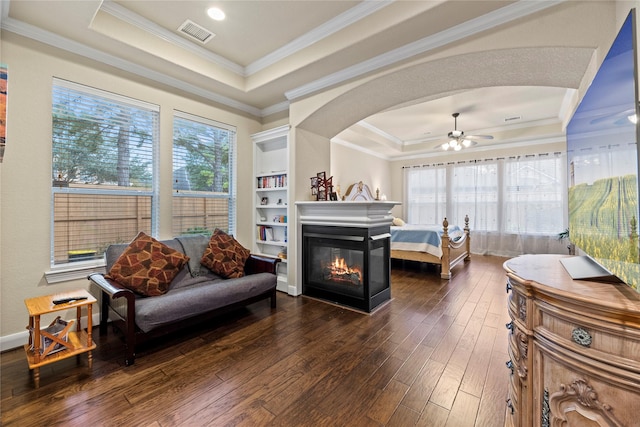 bedroom with a multi sided fireplace, dark hardwood / wood-style floors, a tray ceiling, and multiple windows