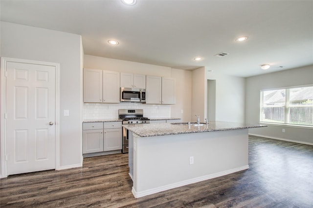 kitchen with tasteful backsplash, dark hardwood / wood-style floors, a center island with sink, appliances with stainless steel finishes, and light stone counters