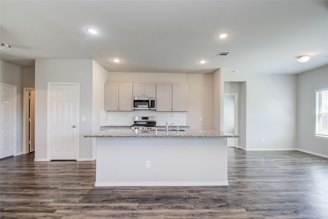 kitchen featuring decorative backsplash, light stone counters, stainless steel appliances, and a center island with sink