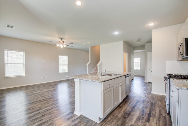 kitchen with light stone countertops, appliances with stainless steel finishes, sink, and a center island with sink