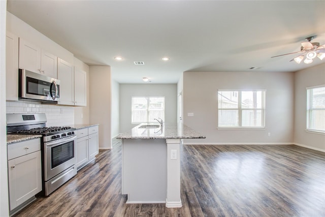 kitchen featuring light stone countertops, white cabinetry, stainless steel appliances, sink, and a center island with sink