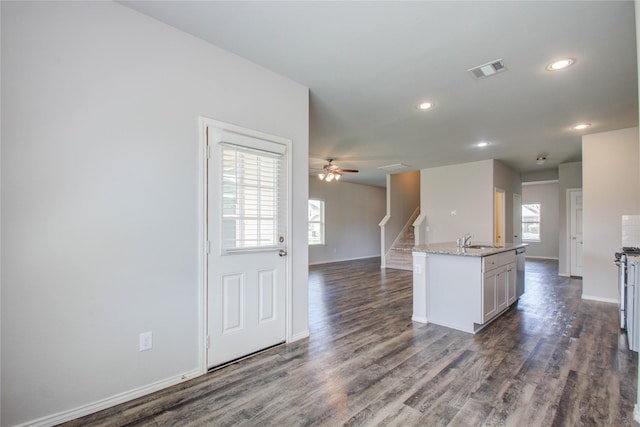 kitchen with stainless steel dishwasher, sink, an island with sink, dark hardwood / wood-style flooring, and light stone counters