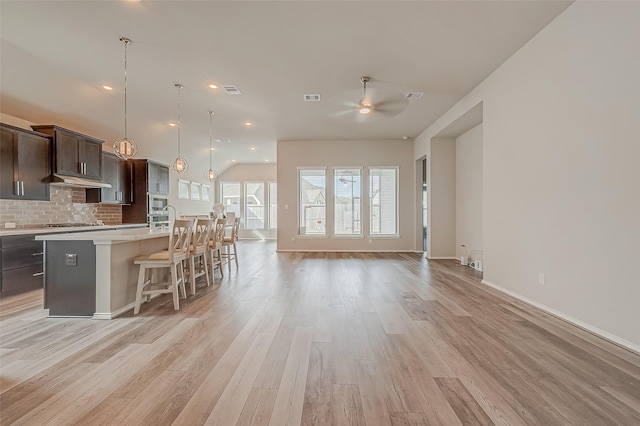 kitchen featuring tasteful backsplash, ceiling fan, a center island with sink, dark brown cabinetry, and a kitchen breakfast bar