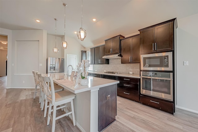 kitchen featuring appliances with stainless steel finishes, dark brown cabinetry, a center island with sink, and hanging light fixtures