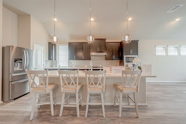 kitchen featuring stainless steel appliances, decorative backsplash, hanging light fixtures, a center island with sink, and dark brown cabinets