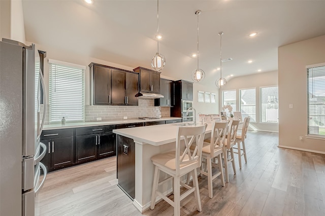 kitchen featuring pendant lighting, appliances with stainless steel finishes, an island with sink, a kitchen breakfast bar, and backsplash