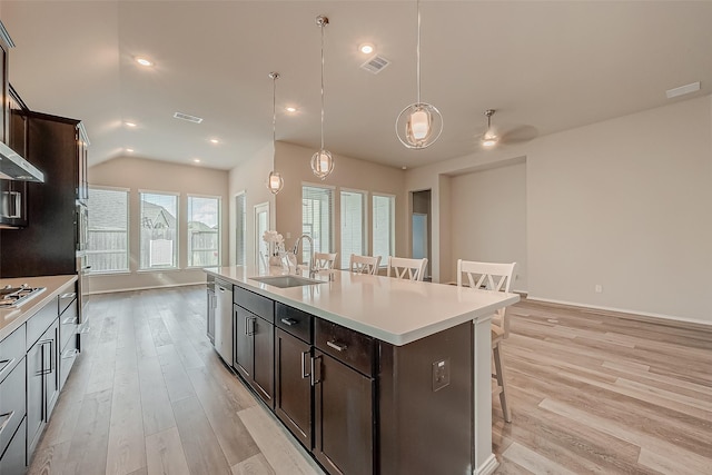 kitchen with pendant lighting, light hardwood / wood-style floors, sink, a kitchen breakfast bar, and a kitchen island with sink