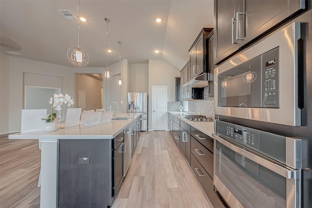 kitchen featuring a center island with sink, appliances with stainless steel finishes, decorative backsplash, decorative light fixtures, and sink