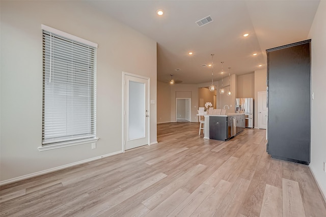 kitchen with decorative light fixtures, light wood-type flooring, an island with sink, a breakfast bar area, and stainless steel fridge