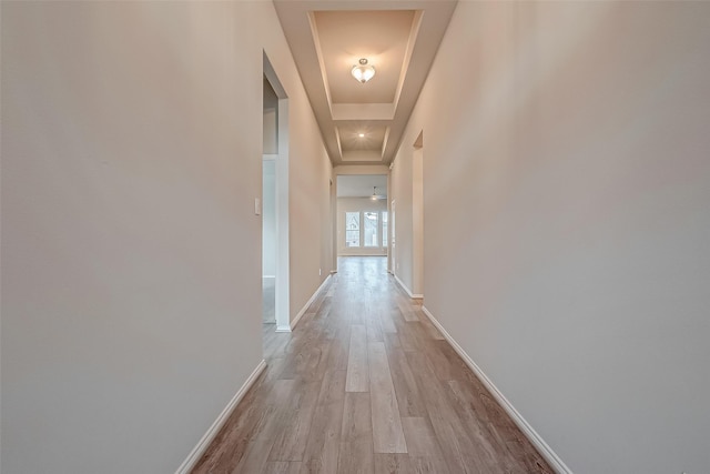 corridor with light hardwood / wood-style floors and a tray ceiling