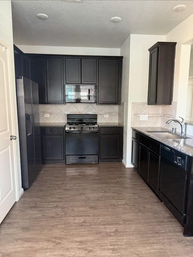 kitchen featuring tasteful backsplash, light wood-type flooring, light stone countertops, black appliances, and sink